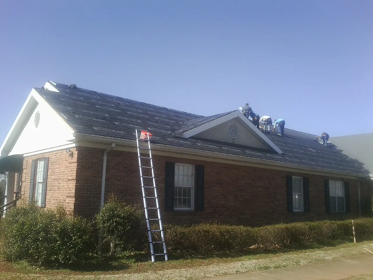 Crew tearing shingles off a brick ranch roof with a ladder set — Metal Roof Repair work by our crew in New Albany