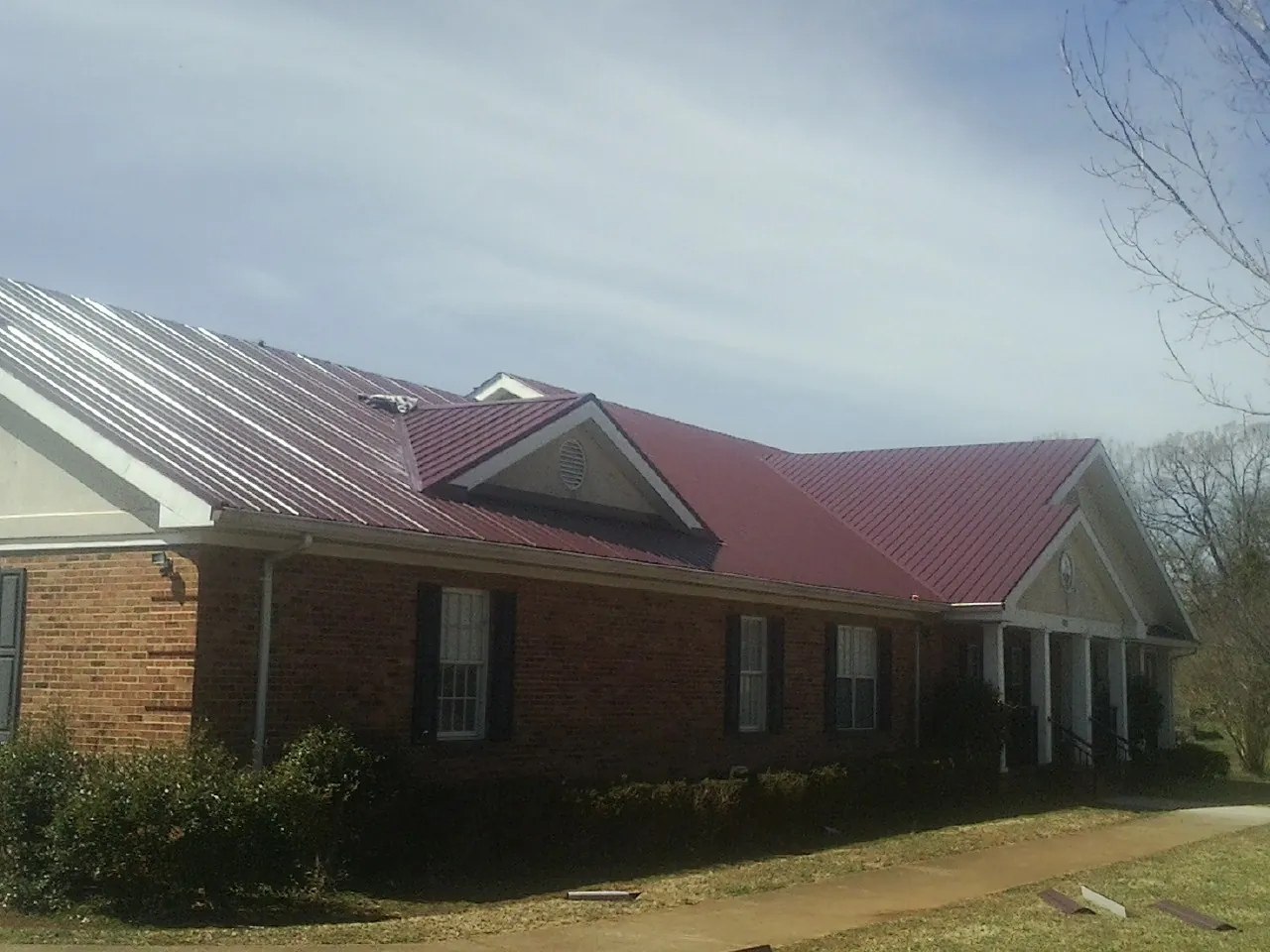 Red metal roof with gabled entries on a long brick building, from a Hail Damage Roof Repair job in New Albany