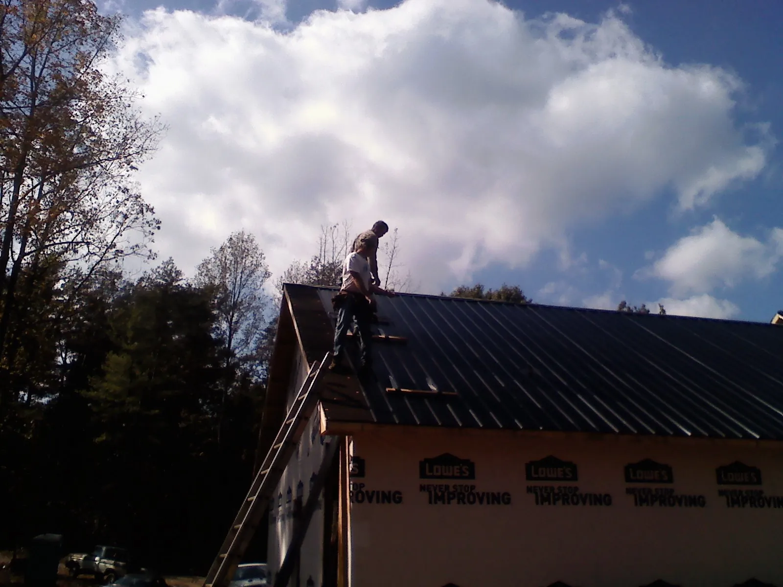 Roofer fastening dark metal panels high against a cloudy sky, from a Roof Inspection job in New Albany