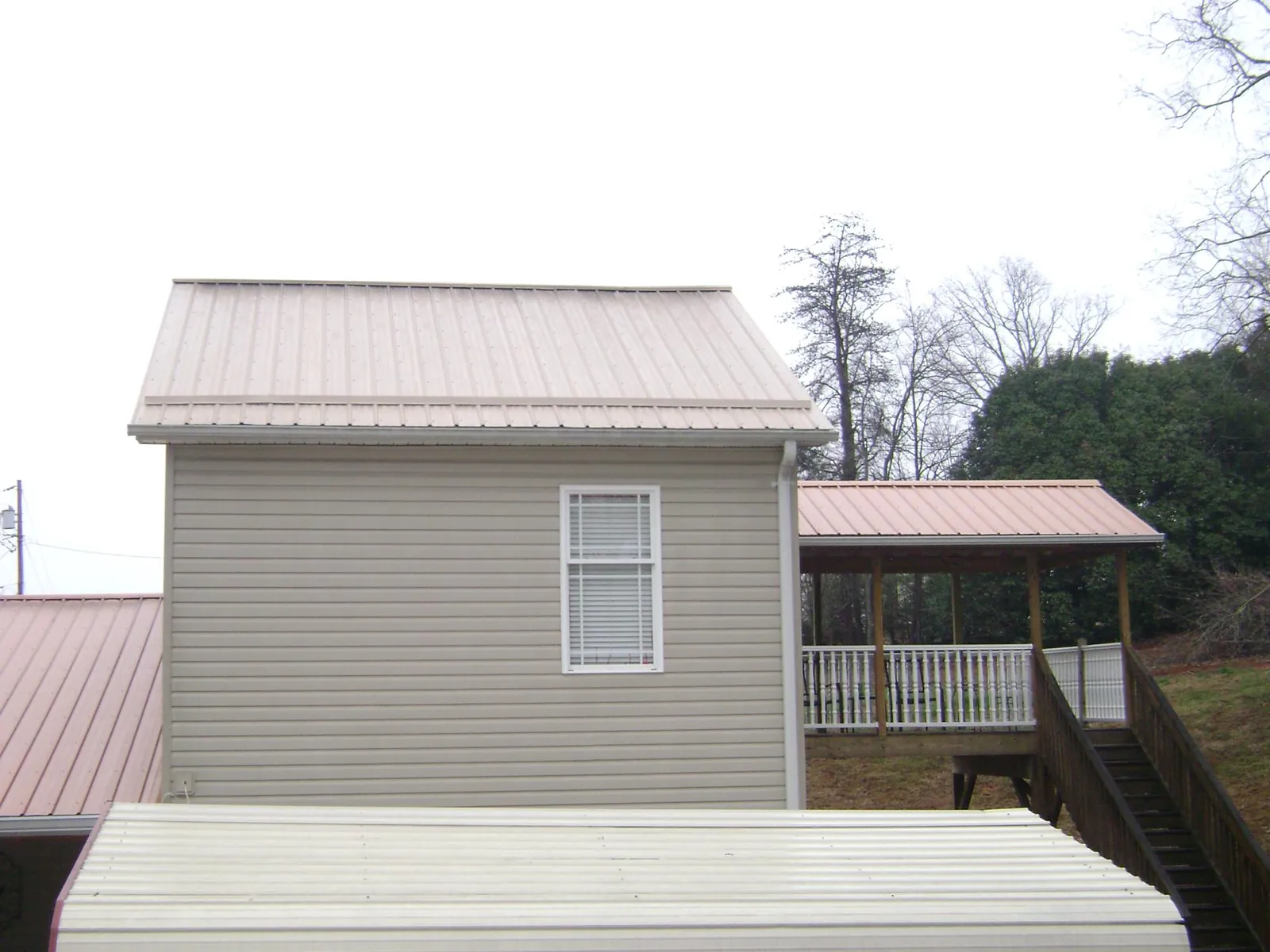 Tan metal roofs on a two story addition and attached porch, from a Roof Replacement job in New Albany