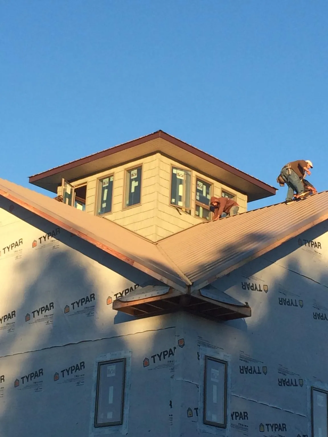 Roofers working around a rooftop cupola on a new metal roof at sunset in New Albany
